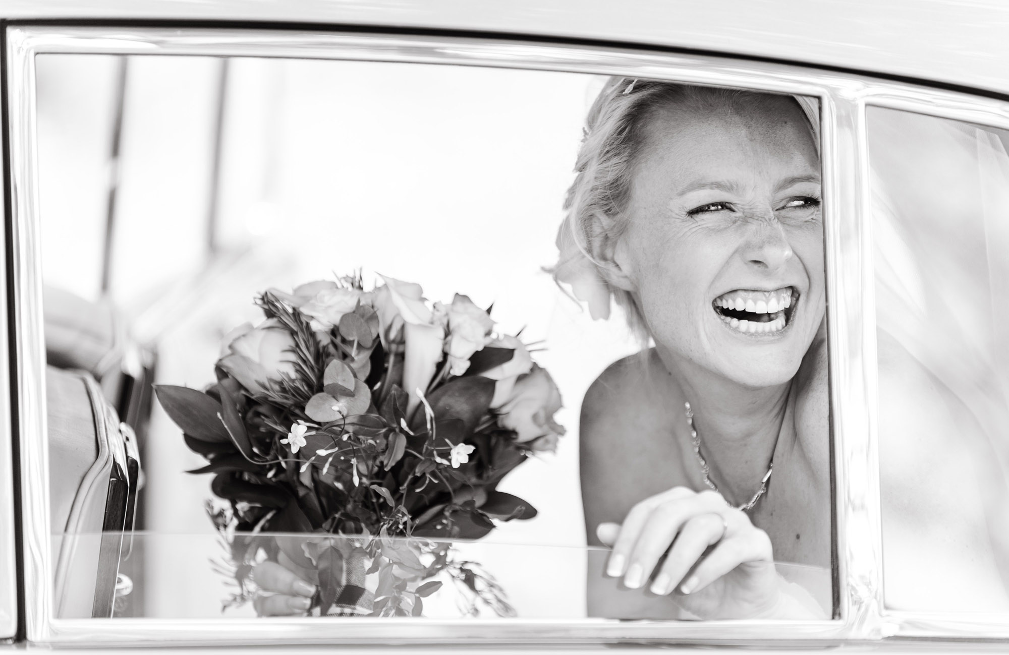 Bride smiles as she arrives by car on the day of her wedding taken by Surrey based wedding photographer Richard Eaton. 