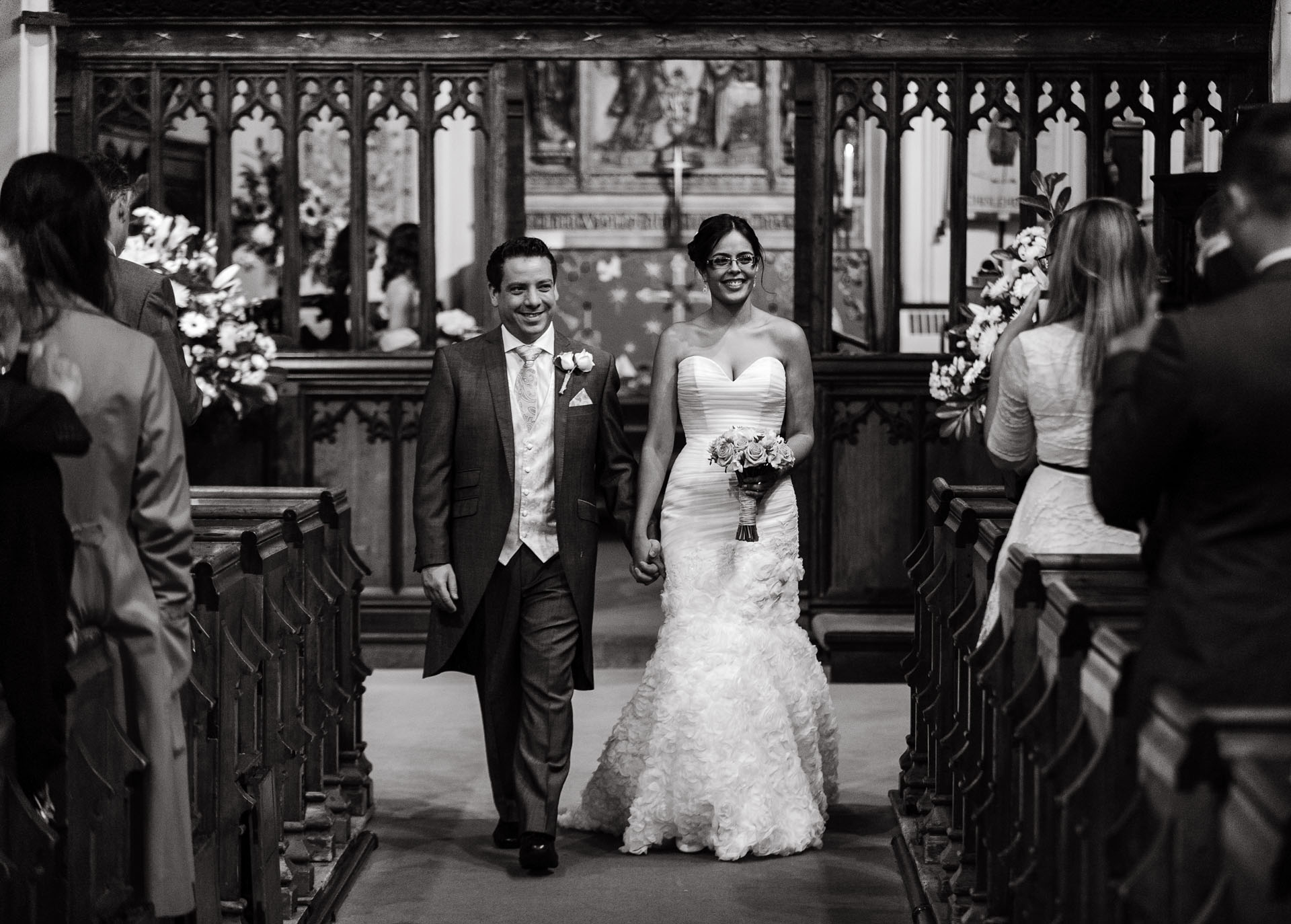 Black and white photograph of a couple walking down the aisle of a church after their wedding ceremony taken by wedding photographer Richard Eaton.