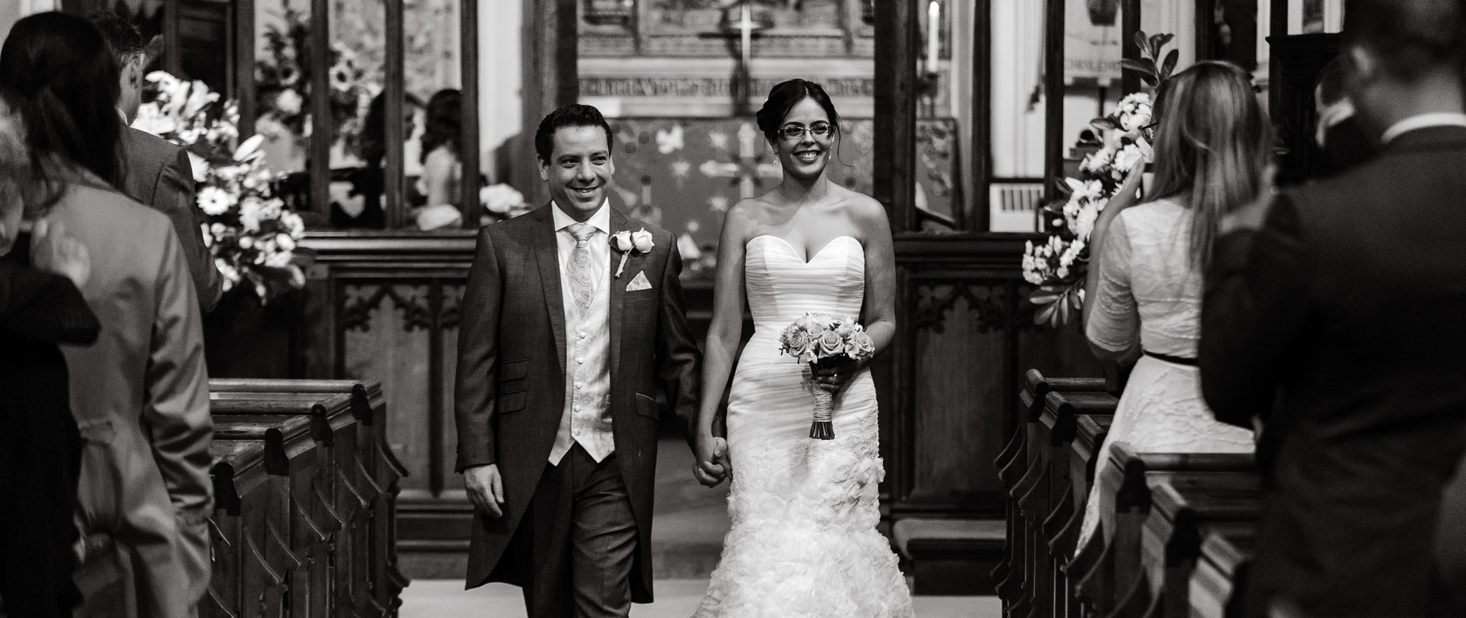 Black and white photograph of a newly married couple walking down the isle of a church taken by wedding photographer Richard Eaton.